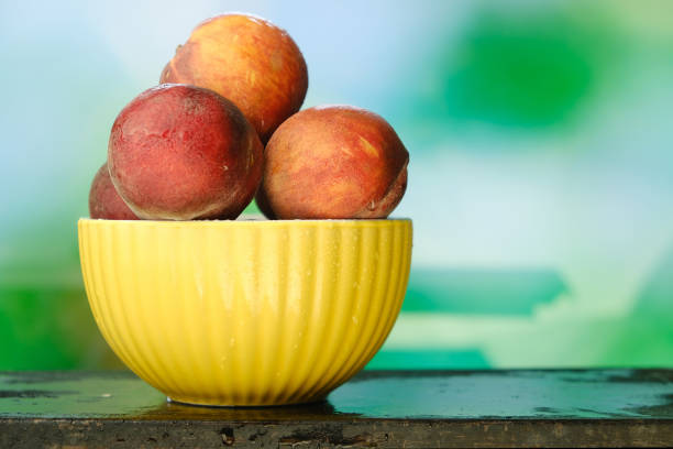 Peaches in bowl on natural green background.