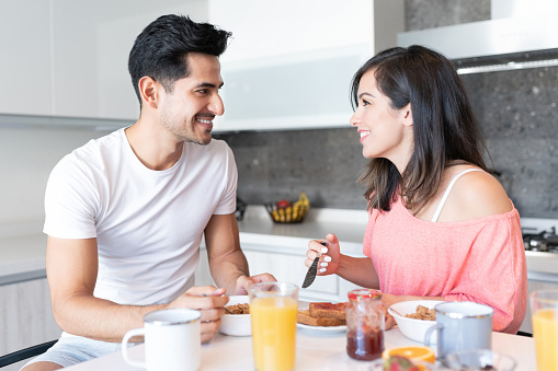 Smiling Latin young couple looking at each other while having breakfast in kitchen