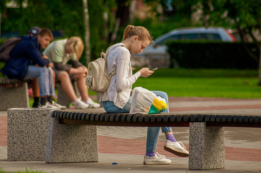 Saint Petersburg, Russia - 22 Augusr 2019. Young girl sits on a bench and looks into the phone