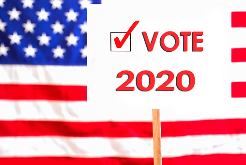 Vote 2020 signs with check box and American Flag Background.  Ballot Box also pictured.