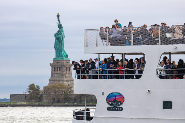 turistas visitando a estátua da liberdade e a ilha ellis em um barco turístico com a estátua da liberdade ao fundo. - statue liberty statue of liberty ellis island - fotografias e filmes do acervo