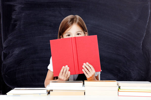 istock Young cute girl sitting at the table and reading a book 1266338766