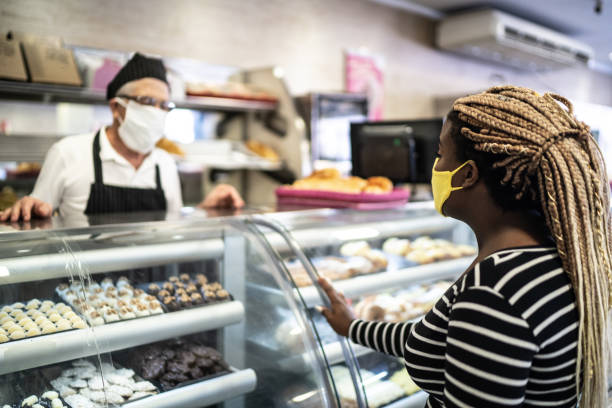 Young woman ordering some groceries in the bakery using face mask Young woman ordering some groceries in the bakery old candy store stock pictures, royalty-free photos & images