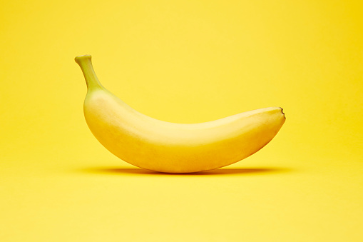 Single fresh raw clean isolated one alone horizontally oriented yellow banana on the bright solid yellow fond background