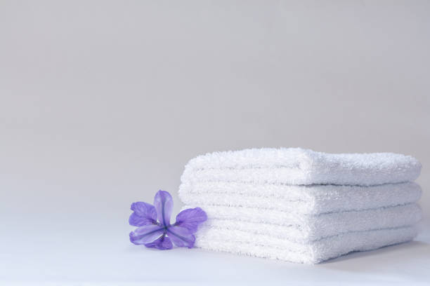 Two white neatly folded terry towels with a purple iris flower on a light background