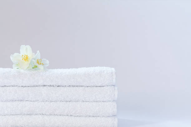 istock Four white neatly folded terry towels with a jasmine flower on a light background. 1266340795