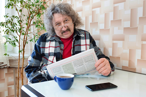 A portrait of an elderly pensioner reading a newspaper at home with a cup of coffee.