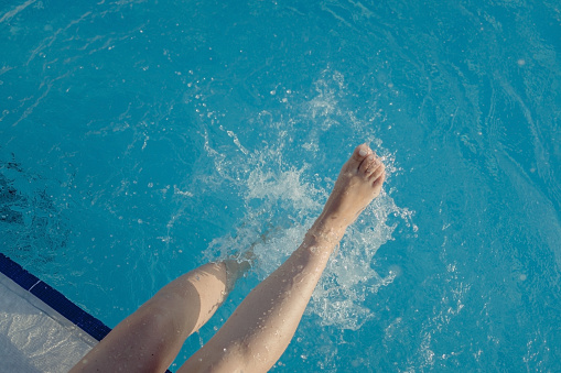 cropped young european woman kicks in the pool splashes water. Concept, carefree, summer, vacation. Copy space. View from above.