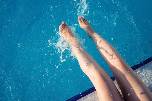 cropped young european woman kicks in the pool splashes water. Concept, carefree, summer, vacation. Copy space. View from above.