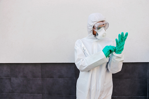 Man in sterile protective uniform standing outdoors and putting rubber gloves on. Protection form spreading corona virus concept.
