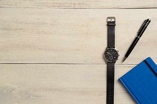 A mechanical wrist watch, a diary and a pen lie on the right on a light wooden table