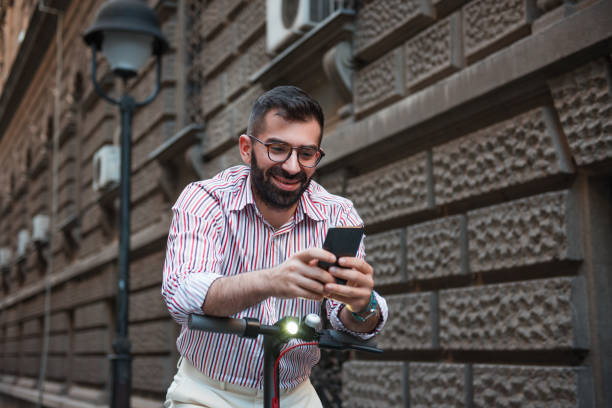 istock Young man with an electric push scooter texting message on his phone while standing on the city street 1266345600