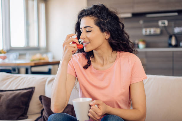 istock Young woman sitting on the sofa and using allergy inhaler 1266361479