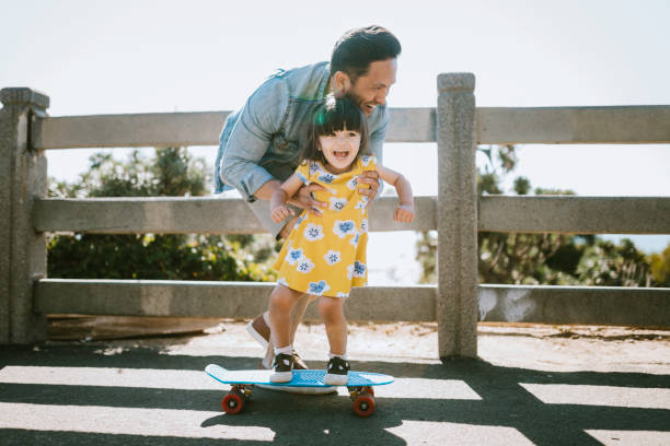 отец помогает молодой дочери ездить скейтборд - skateboard skateboarding outdoors sports equipment стоковые фото и изображения