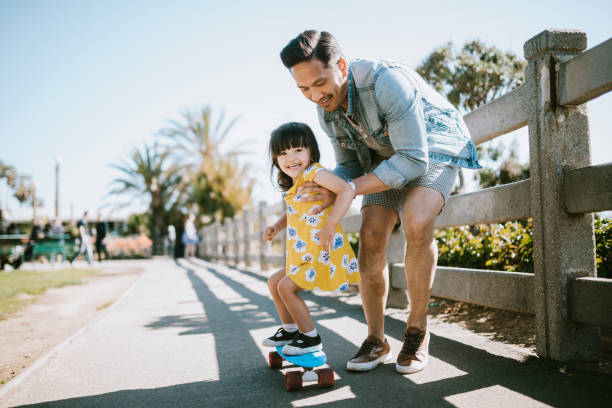 padre ayuda a la joven hija ride skateboard - alegre fotos fotografías e imágenes de stock
