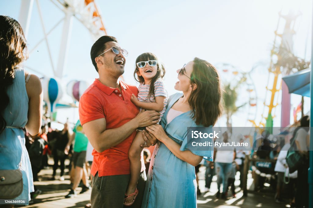 Family Has Fun at Outdoor Carnival Setting A cute mixed race family enjoys the rides and sun at the fair activities on Santa Monica Pier in Los Angeles, California.   They all wear sunglasses with big smiles. Family Stock Photo