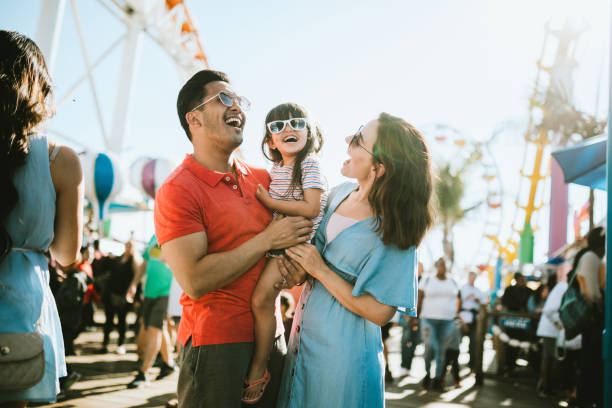Family Has Fun at Outdoor Carnival Setting A cute mixed race family enjoys the rides and sun at the fair activities on Santa Monica Pier in Los Angeles, California.   They all wear sunglasses with big smiles. holiday event photos stock pictures, royalty-free photos & images