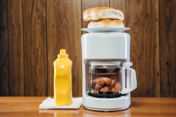 Hot Dogs in Coffee Maker Food Hack A rather disgusting looking office trick for a meal; hot dogs heat in the coffee machine carafe while buns warm on top of the machine.  Retro wood paneling decor in the background. grotesque stock pictures, royalty-free photos & images