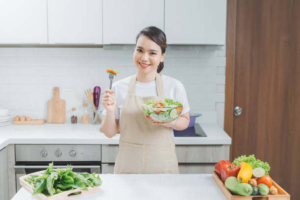istock Young woman eating fresh salad in modern kitchen 1266383827
