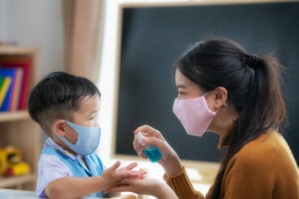 Asian teacher use bottle spray to spray alcohol liquid to hands of her student for prevent corona virus covid 19 in in her class room Asian teacher use bottle spray to spray alcohol liquid to hands of her student for prevent corona virus covid 19 in in her class room, in preschool. korean baby stock pictures, royalty-free photos & images
