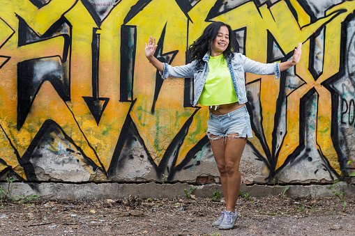 Young cheerful girl in a denim suit and a bright T-shirt is dancing on the background of a wall with a yellow graffiti pattern