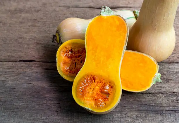 Butternut squash whole and sliced on a wooden table. Butternut is a bell-shape fruit with sweet orange-yellow flesh.
