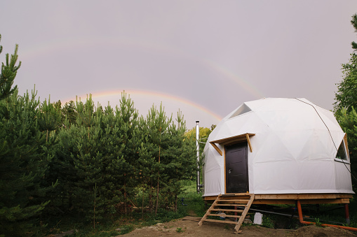 Geodome in pine forest, beautiful semicircular rainbow in the sky after rain