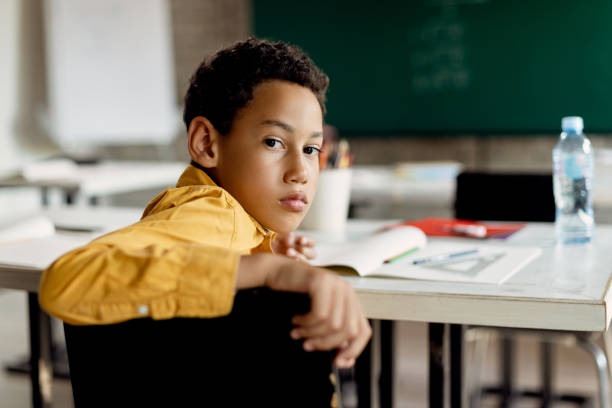 istock Black schoolboy turning to camera while sitting in the classroom. 1266398770
