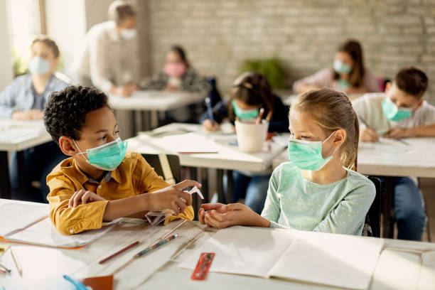 istock Two classmates with face masks sharing hand sanitizer in the classroom. 1266399546
