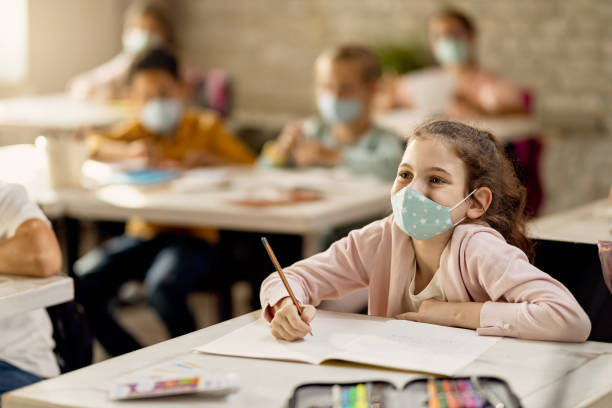 istock Happy schoolgirl wearing a face mask while having a lecture in the classroom. 1266399600