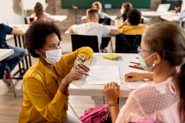 black teacher with a face mask explaining exam results to elementary student in the classroom. - teachers school student imagens e fotografias de stock