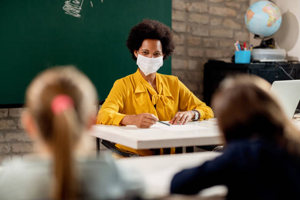 小学校で生徒に話しかける保護フェイスマスクを持つ幸せな黒人教師。 - elementary school elementary student education caucasian ストックフォトと画像