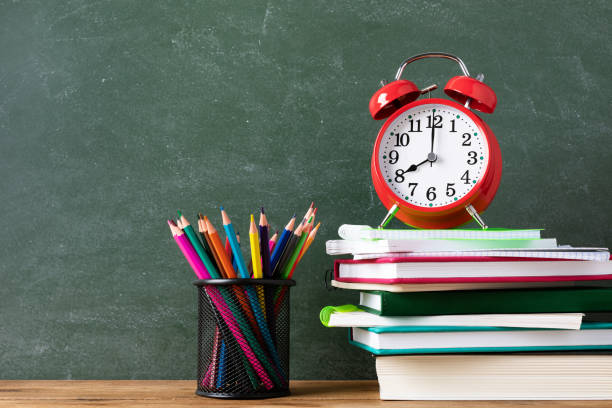 istock Education and learning background with red alarm clock and paper notebooks with colorful pencils against blackboard. Back to school concept. 1266403642