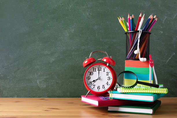 istock Back to school or education creative concept with red alarm clock, colorful notebooks and school supplies against blackboard. 1266403658