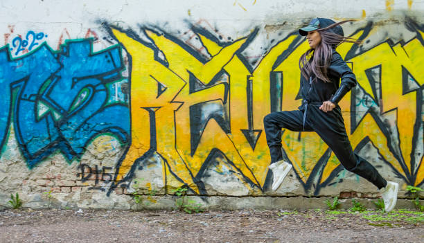 검은 색 바지를 입은 어린 소녀가 스포츠를 위해 들어가 그래피티 패턴이있는 벽의 배경에 달려 있습니다. - child graffiti grunge city 뉴스 사진 이미지