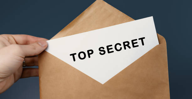 istock Male hand holding craft envelope with text TOP SECRET on blue background 1266406437