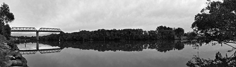 Reflection of a tall pedestrian and water pipe bridge, trees and blue sky on a river, Parramatta river, Rydalmere, Sydney, New South Wales, Australia