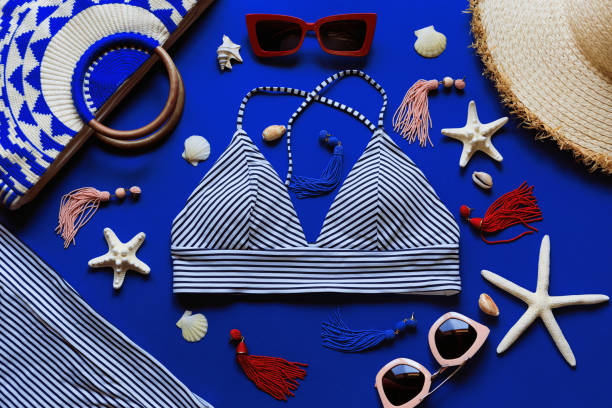 istock Woman's beach accessories: bikini, bag, straw hat, sunglasses, earrings, starfish and shells on electric blue background 1266411930