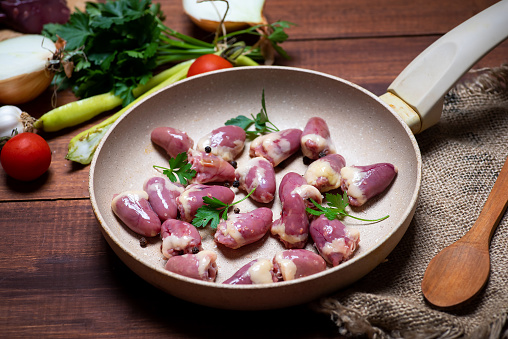 Fresh chicken heart on a ceramic frying pan with cooking ingredients tabletop view