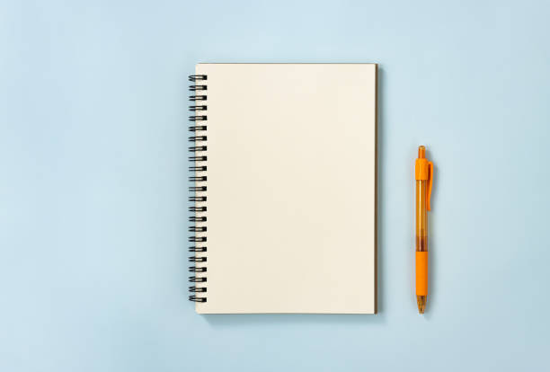 istock Spiral Notebook or Spring Notebook and Orange Pen on Pastel Minimalist Background 1266413193