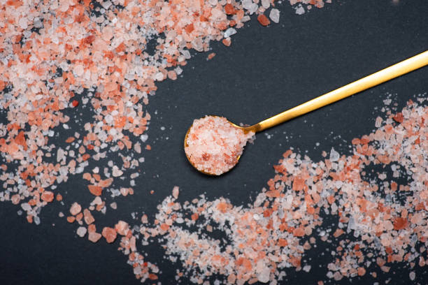 sal de cristal rosa del himalaya sobre una cuchara dorada rodeada de sal sobre una mesa - salt crystal spoon food fotografías e imágenes de stock