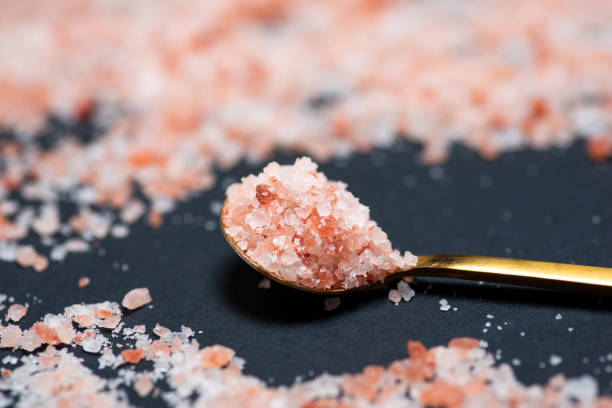 sal de cristal rosa del himalaya sobre una cuchara dorada rodeada de sal sobre una mesa - salt crystal spoon food fotografías e imágenes de stock