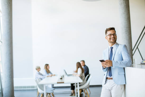istock Happy young man using his mobile phone and smiling while his colleagues working in the background 1266414041