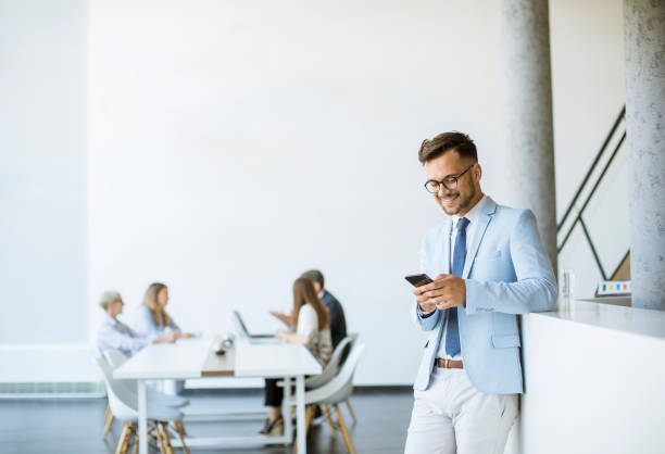 istock Happy young man using his mobile phone and smiling while his colleagues working in the background 1266414058