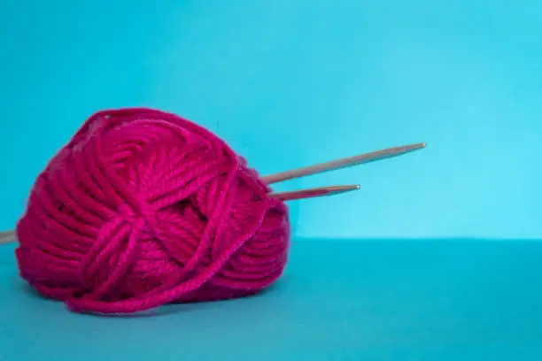 Pink woolen yarn and metal knitting needles on blue background.