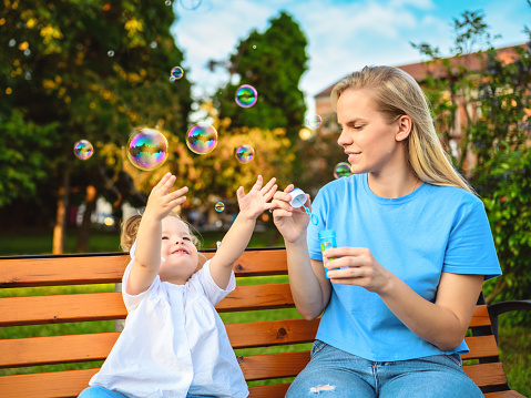 Shot of a happy young mother and daughter blowing bubbles in the park