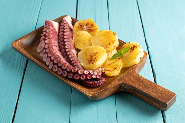 Cooked octopus with potatoes, on serving board, blue wooden background