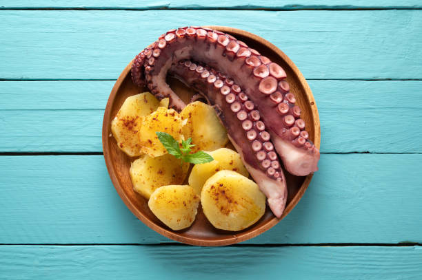 istock Cooked octopus with potatoes, on black plate and blue wooden background, top view 1266417976