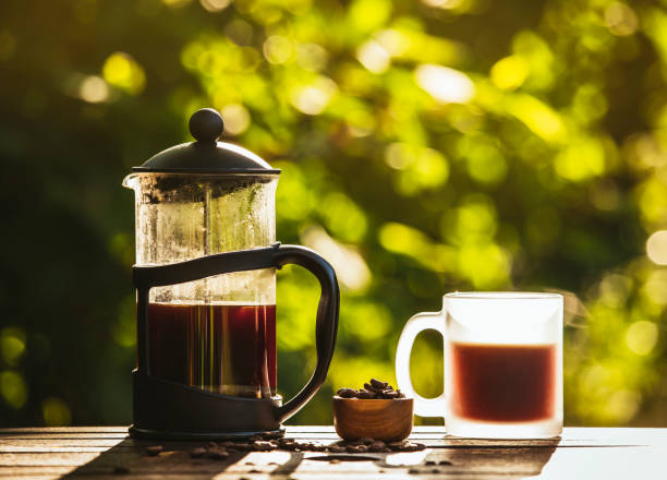 istock French press coffee and cup on table with scattered coffee beans in garden on sunny bright morning day. Reason to wake up concept. Bokeh green background with room for text. 1266425898