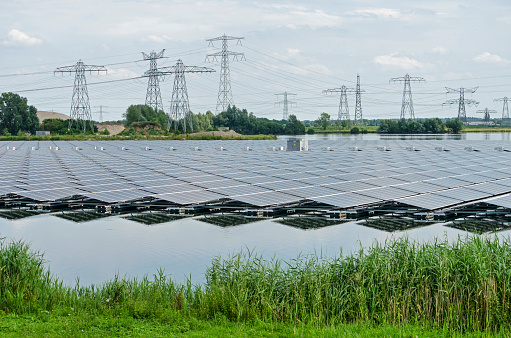 Zwolle, The Netherlands, July 19, 2020: a large array of solar panels reflects in the artificial lake Sekdoorne Plas, with electricity pylons and power lines in the background